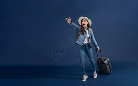 快乐的亚洲青年妇女带着行李以蓝色背景迅速前往机场携带背包车并戴耳机假日和期旅行游概念欢乐的亚洲年轻妇女兴奋的乘客保持旅游高清图片素材