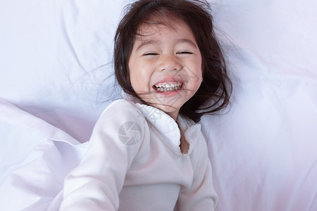 拥抱早晨年轻的上躺在床柔软枕头欢笑着开心快乐的亚洲小孩最喜悦的一景闲暇高清图片素材