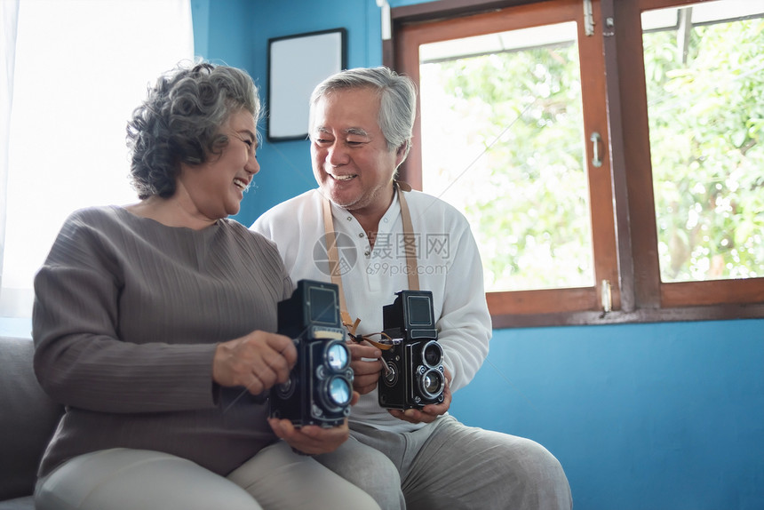 退休时尚有吸引力的笑亚洲老年夫妇享受在家中拥有古老或旧式电影摄机的快乐老人肖像和有传统生活方式的女爱人摄影师共舞浪漫图片