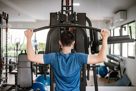 男健身房训练体操概念一名男少年使用体操设备将两只肌肉手臂对着机器拉来去耐力背景图片