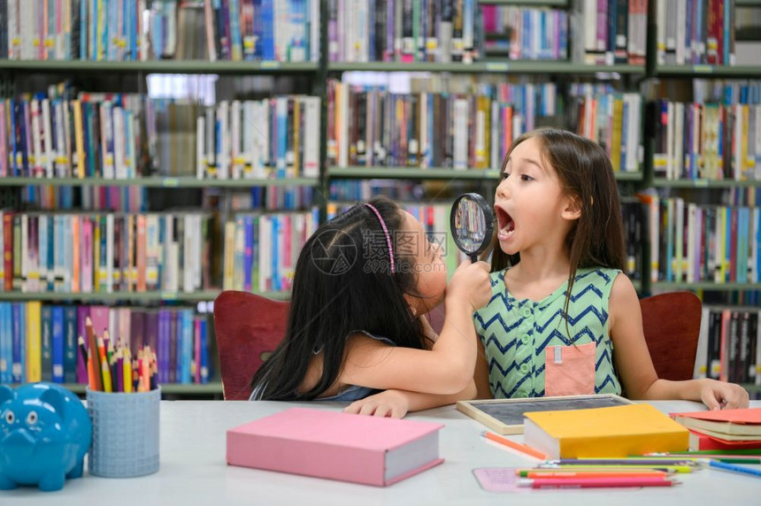 逗在室内两个快乐的小可爱女孩做笑脸和在学校图书馆玩一起作为牙科健康检查教育和自学无线技术人们的生活方式和友谊人们在学习多样图片