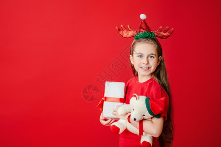 标贴包角白种人孩子一个有趣的快乐女孩肖像头上缠着角绷带抱一只泰迪熊穿着圣诞睡衣背景为鲜红色头抱着一只泰迪熊与鲜红色背景隔开假期背景