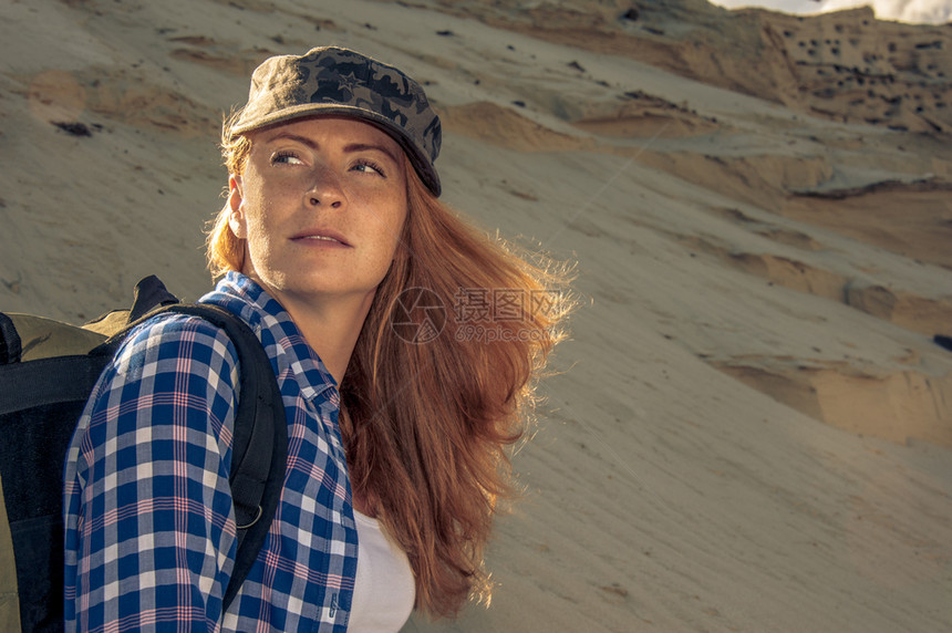 潮人穿着棒球帽的红头发和雀斑在斜坡沙丘上享受日光的格式衬衫以及背包旅行徒步和积极生活方式概念的希斯特女孩在斜坡沙丘上享受太阳的希图片
