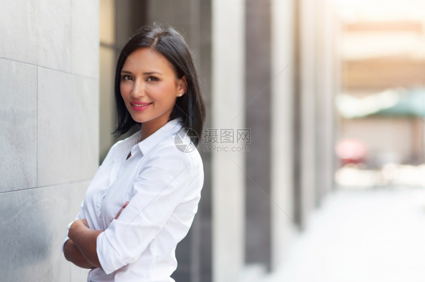 泰国身穿白衬衫自信地站立和复制空间在户外微笑着的美丽女中穿着白色衬衫在建筑背景上看摄影机她满脸双臂交叉常设放松图片