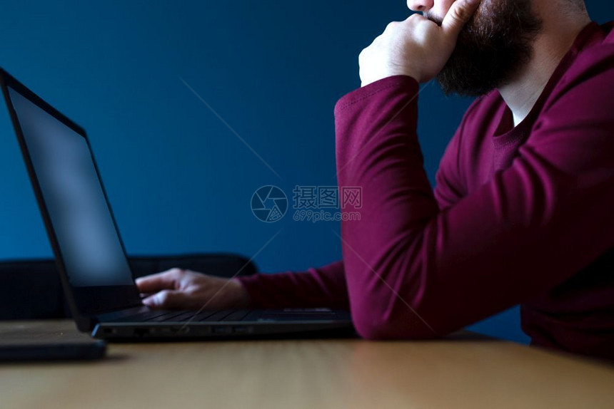 眼镜无线的年轻人在深夜用蓝色背景的笔记本电脑上网用喜怒无常的蓝色和红深夜工作年轻人在深夜用蓝色背景的笔记本电脑上网用喜怒无常的蓝图片