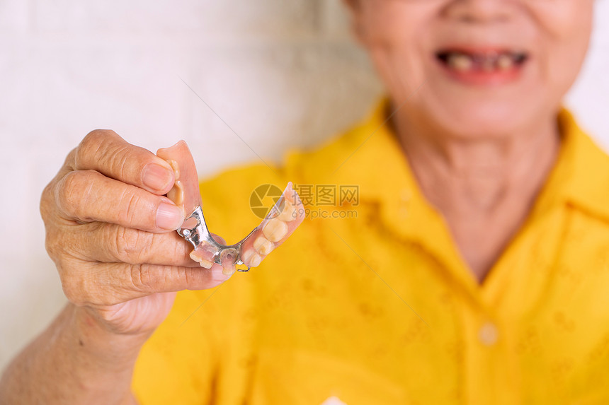 70岁以上的亚洲老年妇女要微笑手持假牙和安装肢置以取代缺失的牙齿并帮助咀嚼食物为替代丢失的牙齿和帮助咀嚼食物而建造的假肢装置健康图片