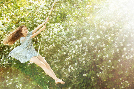 春天女孩荡秋千喜悦只要休闲的快乐美丽女孩在公园里荡秋千在阳光下快乐美丽的女孩在公园里荡秋千在苏背景