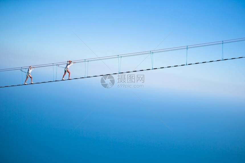 暂停冒险恐惧在山上悬吊桥的小女孩跨越绳桥上的裂缝女孩们图片