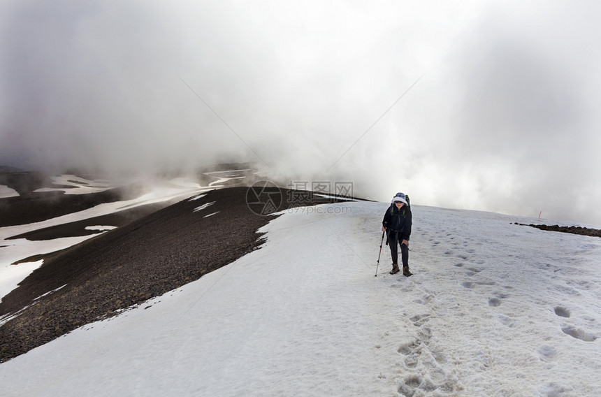 一位背着着一个的旅游妇女手里拿着一个追踪棒前往雪地高山进行一场运动游客从山上爬到雪地顶峰登山戳成就图片