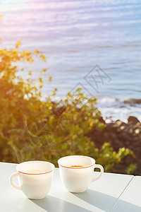 晴天夏在阳台上喝两杯咖啡可以看到大海和岸边的树木阳光明媚的早晨背景柔和焦点阳台上的两杯咖啡可以看到海岸上的洋和树木阳光美丽的早晨放松高清图片素材
