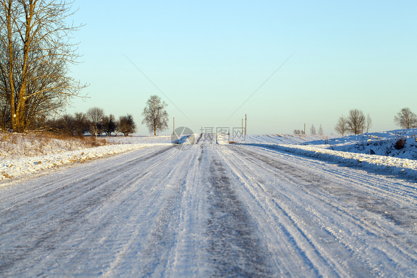 在雪堤表面经过的汽车痕迹可见于积雪公路背景轨迹中的森林和蓝天空在积雪路面上通过车辆的痕迹可见森林和蓝色天空户外寒冷的若冰霜图片