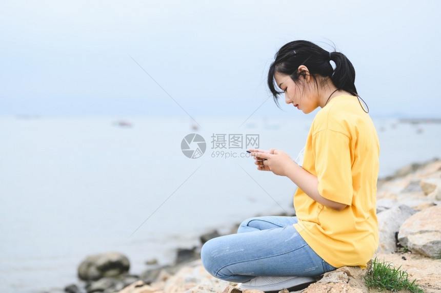 脸在线的亚洲人年轻妇女在海边使用智能手机在接种Covid19或Corona流行疫苗后将面罩除去呼吸新鲜空气人们的生活方式健康概念图片