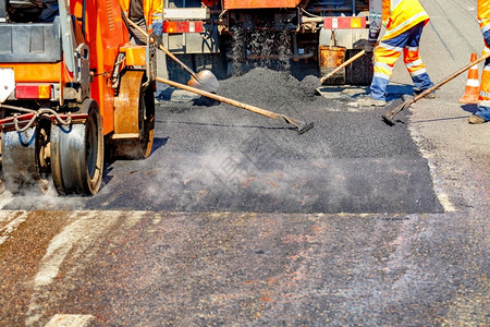 维护机器车轮一组身穿保护橙色制服的公路工人使用铲子平面和小型道路设备修理段复制空间A组道路工人使用手具和道路设备维修段部分公1个路面高清图片素材