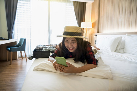 幸福的亚洲旅行者妇女在度假豪华室内卧设计旅游和行概念上睡觉和使用智能手机睡在旅馆或店宿舍卧室的床上并使用智能手机在假日旅行游和概搜索高清图片素材