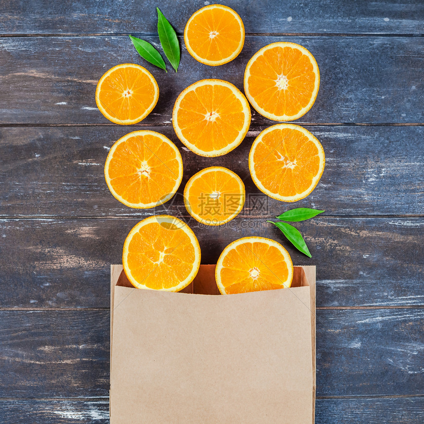 具有创意的黑暗风格平板最顶端展示了棕色木制桌背景手工艺购物袋中新鲜橙子水果切片复制空间为供销售或食谱书用的最小夏季鲜柑橘制品或配图片