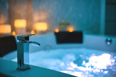 房间休息水疗按摩浴缸特写水龙头中的蓝色冒泡水背景上装饰着蜡烛放松和生活方式抽象背景蓝色灯光美丽水疗按摩浴缸特写水龙头中的蓝色冒泡镜子高清图片素材