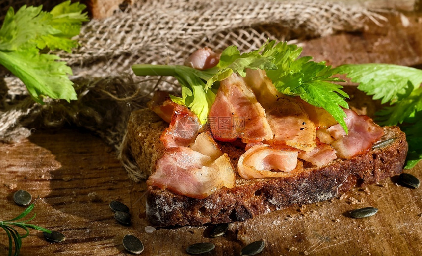 配有培根和菜叶的三明治以及一片黑麦面包上的熏肉和大菜叶由子和南瓜种制成健康食物概念传统手工艺面包缝合一顿饭黑暗的早餐图片