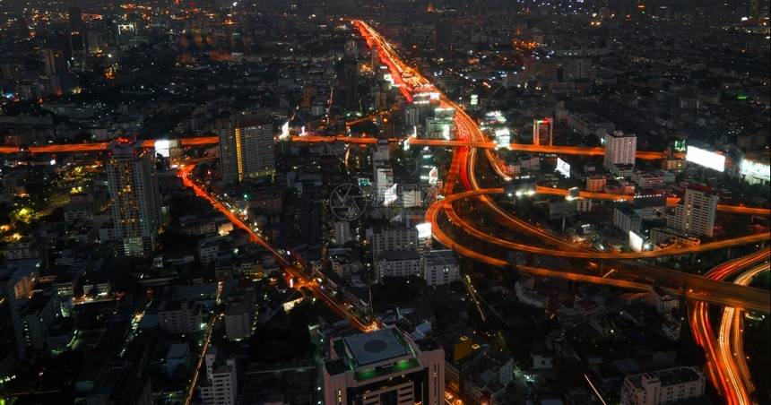 匆忙发光的泰国曼谷街对面的摩天大楼和城市交通灯光照亮的市际夜城景空中视野全观图片