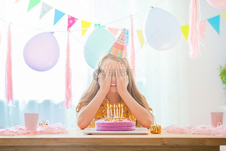 快乐的小女孩在生日派对上许愿希望白种女孩满怀梦想地微笑看着生日彩虹蛋糕喜悦的多彩背景气球生日派对和愿望的概念YLAK停留帽内部的图片