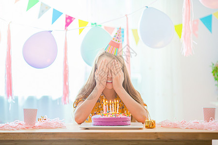 快乐的小女孩在生日派对上许愿希望白种女孩满怀梦想地微笑看着生日彩虹蛋糕喜悦的多彩背景气球生日派对和愿望的概念YLAK停留帽内部的背景图片