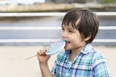年轻的关心有趣小孩吃棒糖快乐的小男孩拿着大糖果孩子笑脸的吃甜食活跃的童年在阳光明媚的夏日享受户外游乐公主不良高清图片素材