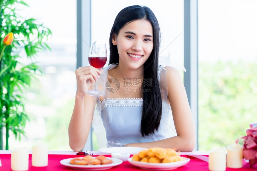 酒精天情人节的概念笑亚裔年轻女坐在餐桌食品展上带着酒杯在餐厅背景中盛着的美酒杯淑女图片