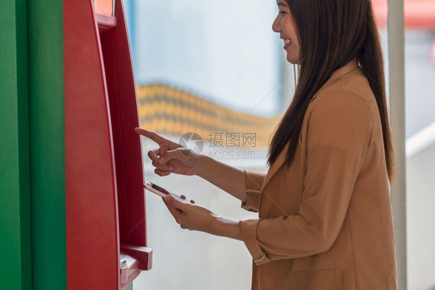 正面美元亚洲人使用智能手机在自动取款前退出自动取款机商业自动取款机概念的女士图片