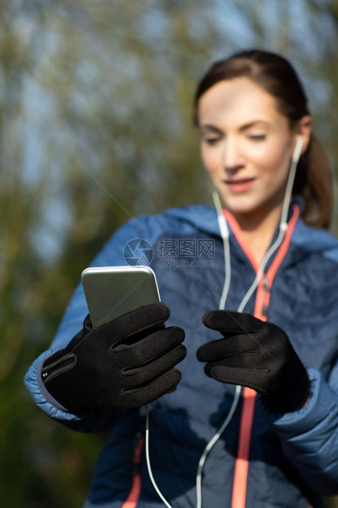 户外锻炼赛跑者年轻女在公园行前选择音乐在移动电话上倾听声音图片