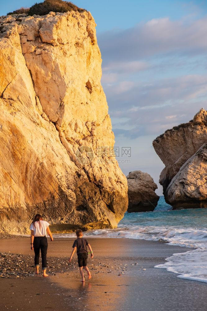 经过考虑的一个男孩和女在海滩上赤脚步行再次在PetratouRomiou岩石上裸浴下午的阳光洗澡在塞浦路斯帕福海滩被认为是希腊神图片