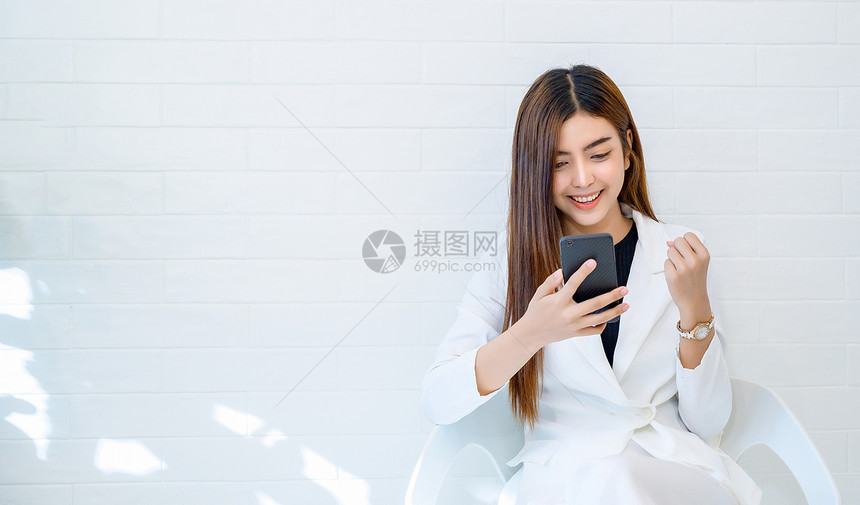 高兴的女商人穿白衣乐于在人背景下玩手机女士衣服图片