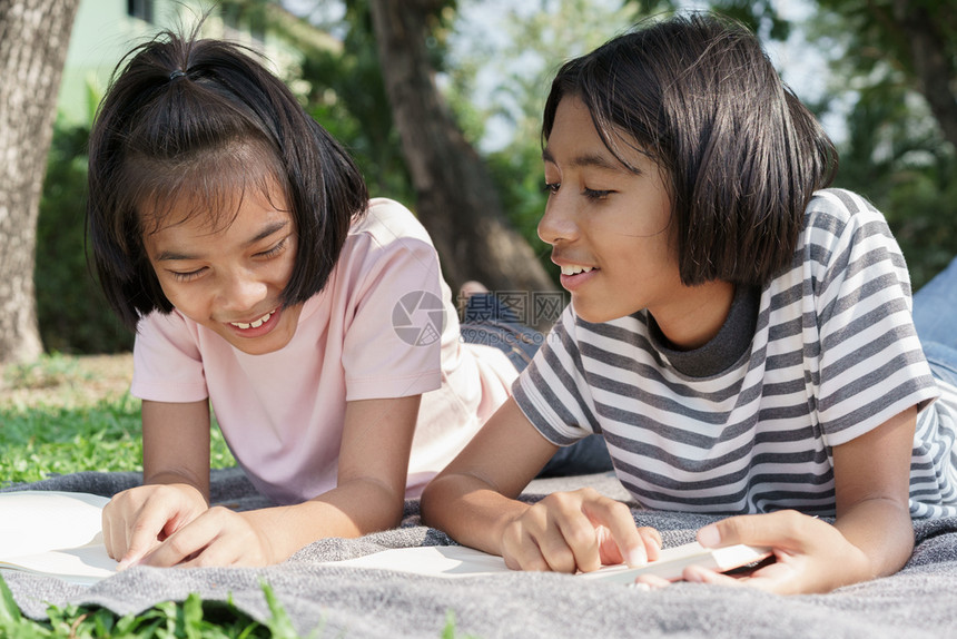 冒险亚洲快乐学生在夏天躺毯子上的阅读书时有两个亚洲女孩在早上公园一起微笑和放松女学生来习野外旅行在户学习笑声晴天随意的图片