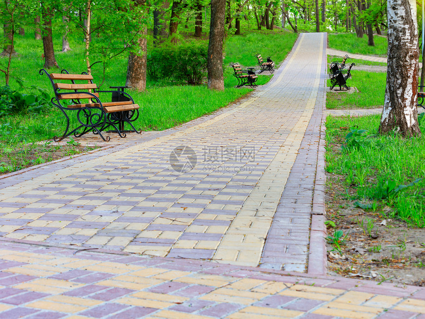 花园舒适小路一座石头铺有木板凳的步行道沿着城市夏季公园大树之间美丽的绿草坪在城市夏季公园中运行同时在一个图片化的城市夏季公园里复图片