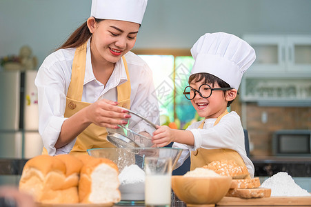 玩面团女人孩子们食物家庭可爱的亚洲小男孩和美丽的母亲在餐桌上的厨房里用筛选器把面粉擦成里有筛子细水沟在厨房里准备烘烤面包店和蛋糕背景