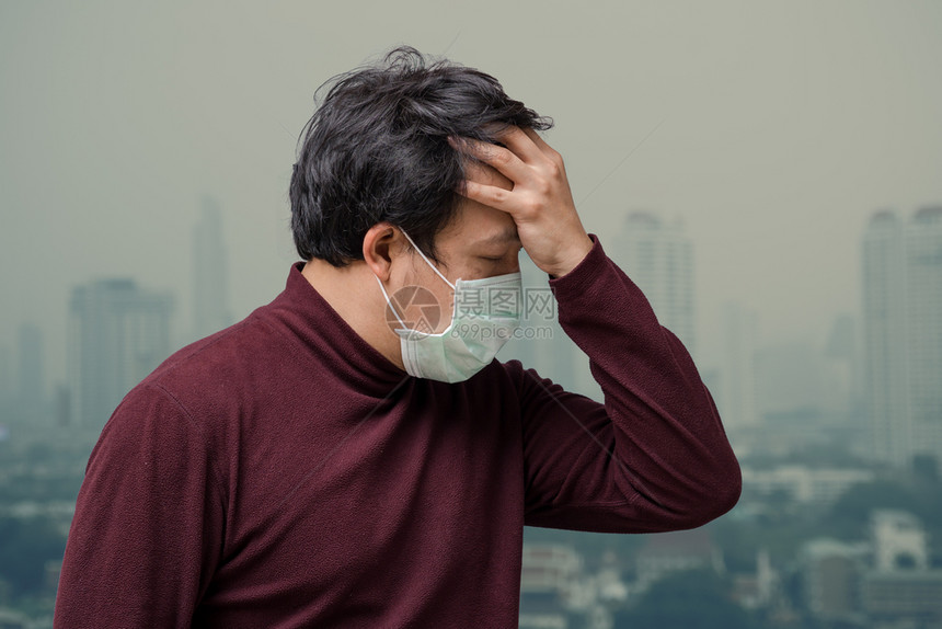 流行病东南身戴面罩的亚裔男子在高公寓阳台上抓头痛在Bangkok市风景背上看到污染和浓雾他戴着面罩防止空气污染感图片