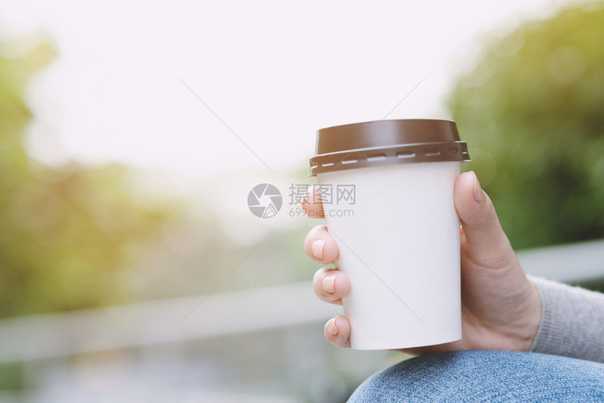 年轻女手握纸杯在自然清晨阳光照亮时喝咖啡用纸杯拿走咖啡为您的文字或标志提供场所清爽瓜拉纳皮户外图片