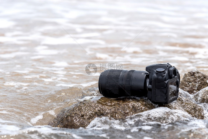 在极端环境旅行和试验时摄影师DSL用DSR相机在海浪的石滩上用探水器湿透了海浪的石滩上摄像头破碎的孤独信号图片