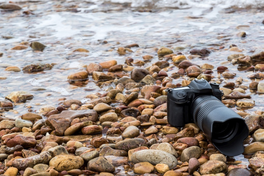 住房黑色的数字在极端环境旅行和试验时摄影师DSL用DSR相机在海浪的石滩上用探水器湿透了海浪的石滩上摄像头图片