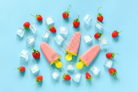 冰棒模具食物菜单棒冰自制明亮塑料模具中的天然冰淇淋蓝色背景的草莓和冰块顶视图平躺自制冰棒背景