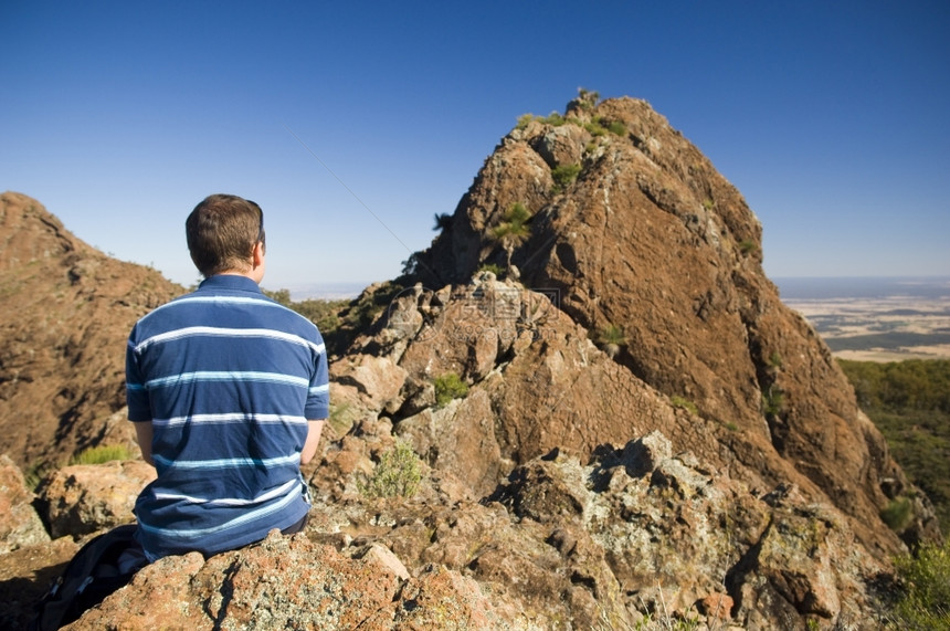 停顿登山者暂休息坐在悬崖顶上俯视前方的山脊棕色流浪汉图片