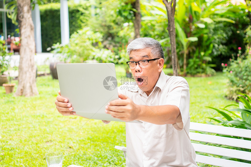 亚洲人有趣的眼镜一名年长亚洲老人拿着电脑笔记本在得到子邮件后惊讶地读到院关于退休没有年龄主义和嗜好的概念消息Ahnication图片