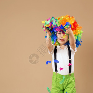明亮的男生美丽快乐小丑男孩用大彩色假发欢快的小丑男孩用丑假跳动玩得开心孩子的肖像扔出一个多彩色的锡子和涂面生日男孩背景图片