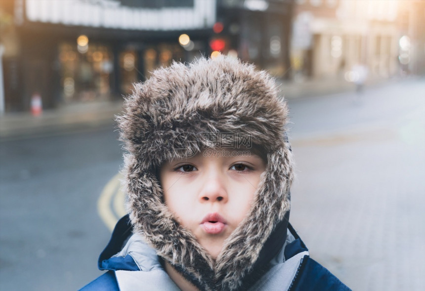 青年情绪化的可爱基德男孩身着毛皮戴面罩的冬季大衣独自站立身上有模糊的光耀眼和灿烂日光闪耀情感肖像儿童晚上在城里街散步时感到寒冷冬图片