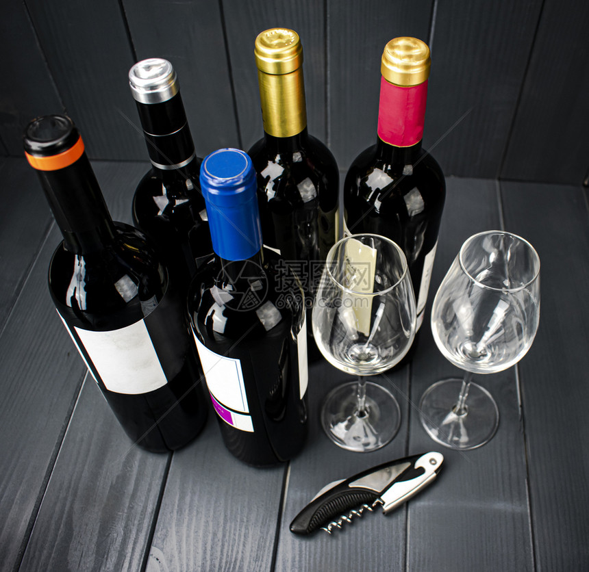 透明水晶来自不同制造商的一瓶红酒配有两杯闪亮葡萄酒眼镜和一瓶用于在明亮灰色木制板空间内调味的软木罐头饮料图片