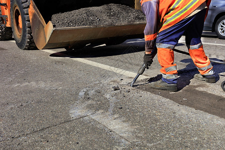 街道路维修工人在施期间用一部手推机将旧沥青从公路上的旧沥青清除出来在道路建设过程中一名工人用台充气大锤清除了一块沥青路面桶团队高清图片素材