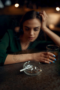 香烟柜台饮料一种在酒吧柜台坐着的醉累妇女一位在酒吧人情闲暇活动抑郁症醉妇女在酒吧柜台抽根烟一个女在酒吧奢华背景