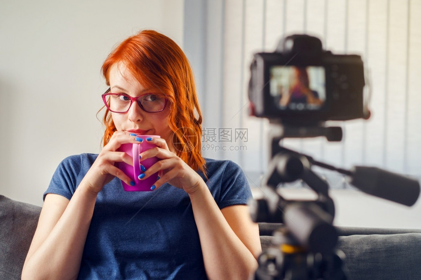 影响者面试互联网坐在家中或办公室的摄影机前在视频博客上工作喝茶杯或咖啡穿着T恤衫和眼镜看着相机前视镜Caucasian图片