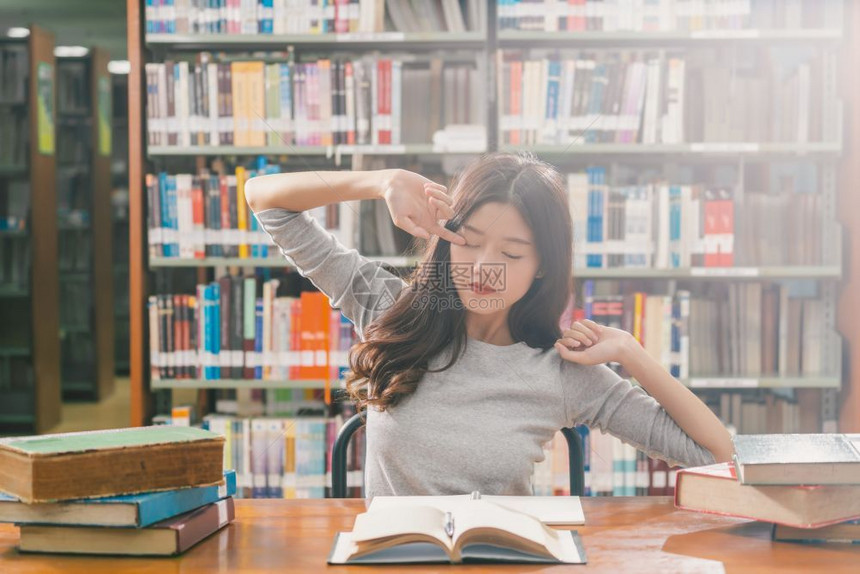 在大学图书馆或群落里阅读和做功课的亚洲青年学生在书架上木制桌子的各种书籍和文具上写着返回学校的书架习人们成图片