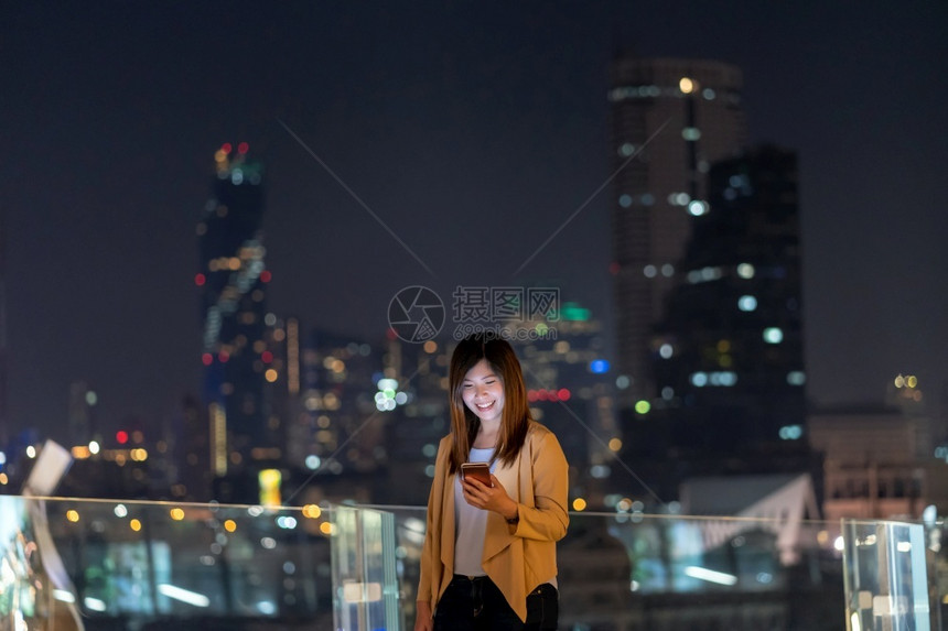 使用智能手机的亚洲女商人在泰国Bangkok河边金融区地使用带微笑动作的智能移电话具有职业概念的技术在Technologywit图片