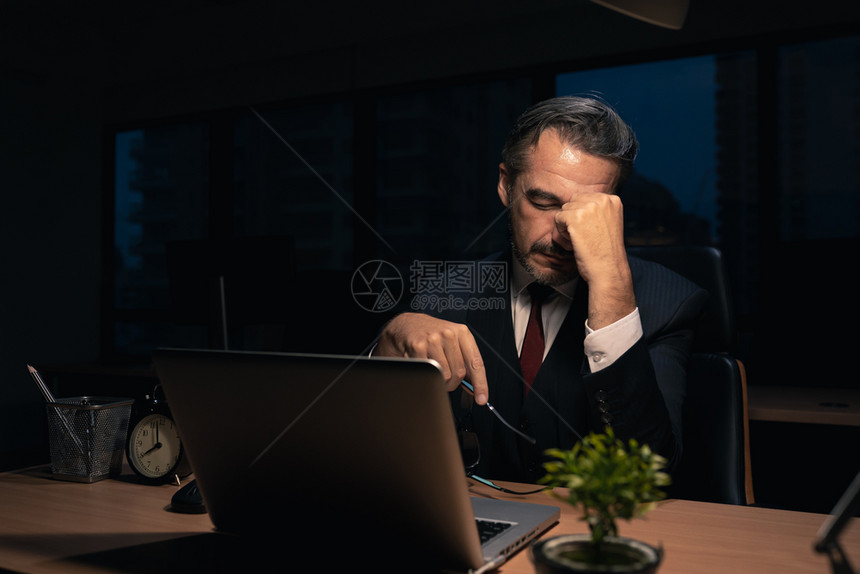 晚的男人高级商在行政主管职位上担任高级男商人晚上班加累经理夜间工作疲劳累在晚间工作人图片