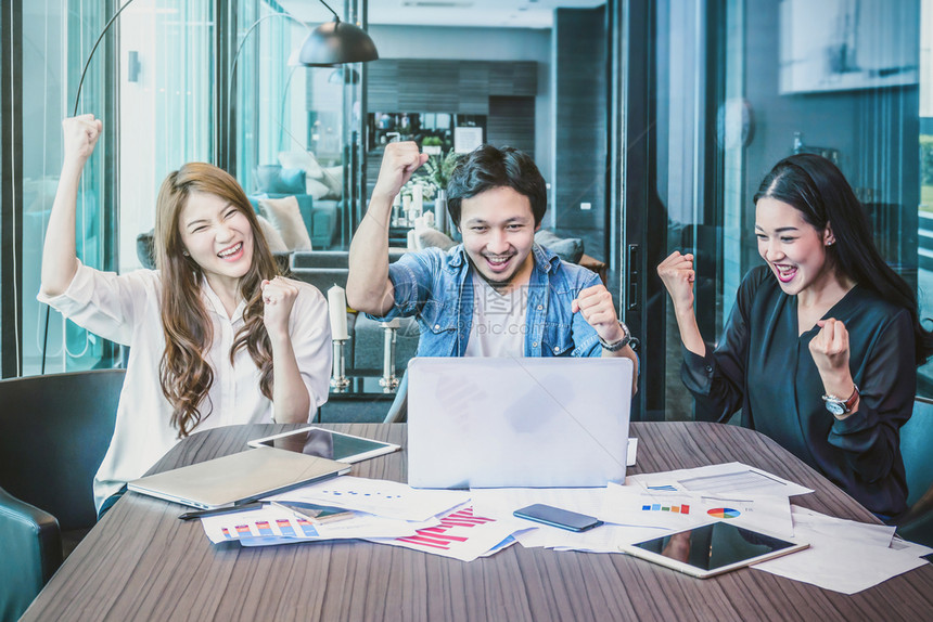 电脑商人随意的亚洲业集团中穿便衣在现代办公室以欢乐的行动和庆祝活开展工作的亚洲商群体人的业团概念图片